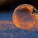 Close-up shot of a frozen bubble with warm reflections resting on a snowy surface at twilight.